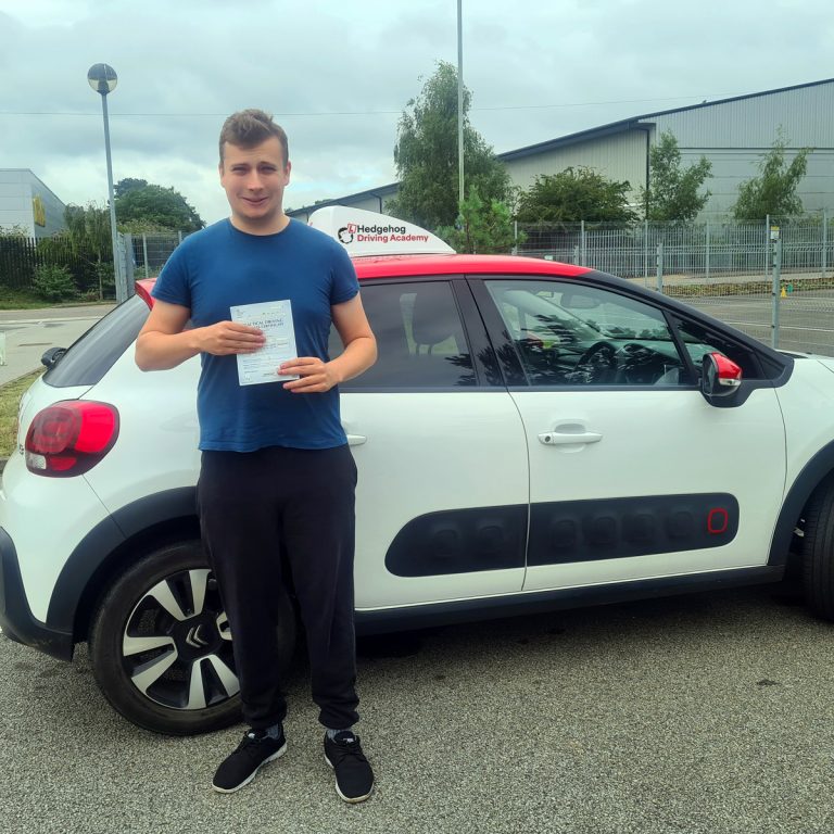 A student holding their pass certificate in front of the Hedgehog Driving Academy car