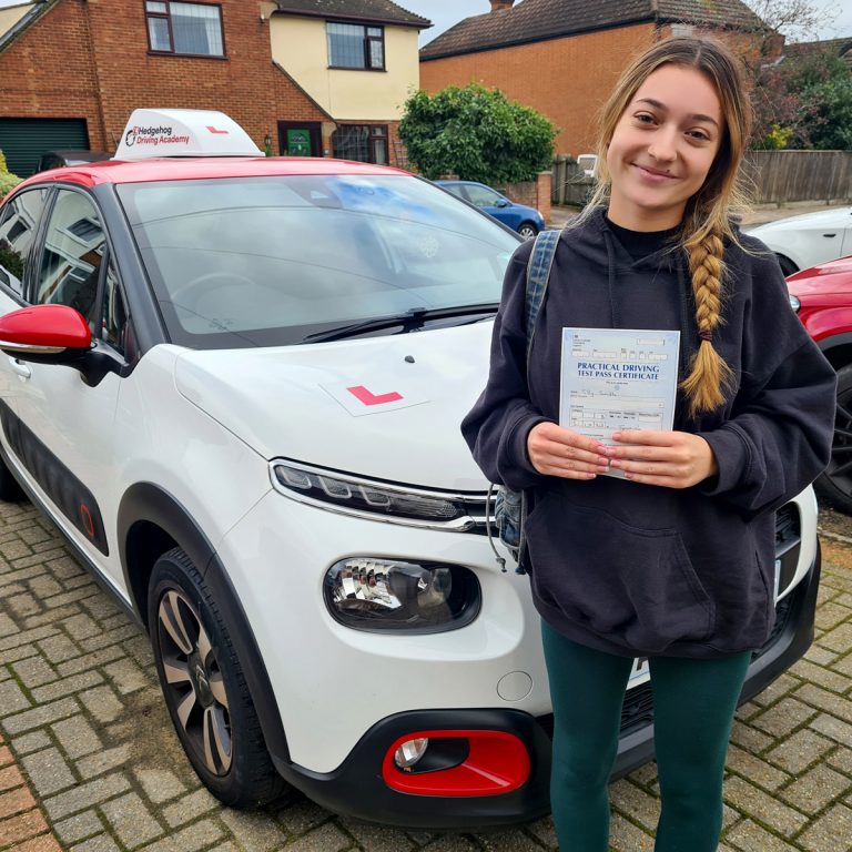 A student holding their pass certificate in front of the Hedgehog Driving Academy car