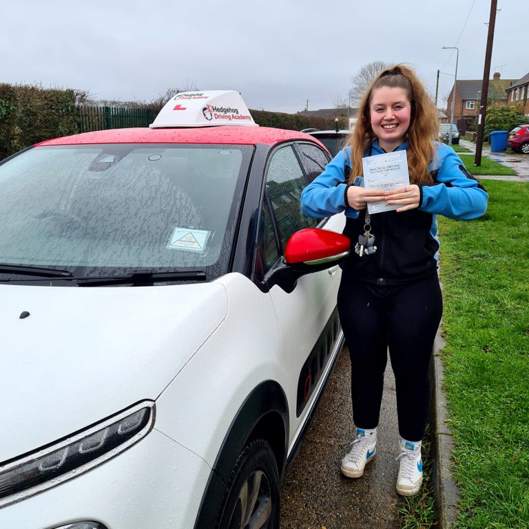 A student holding their pass certificate in front of the Hedgehog Driving Academy car