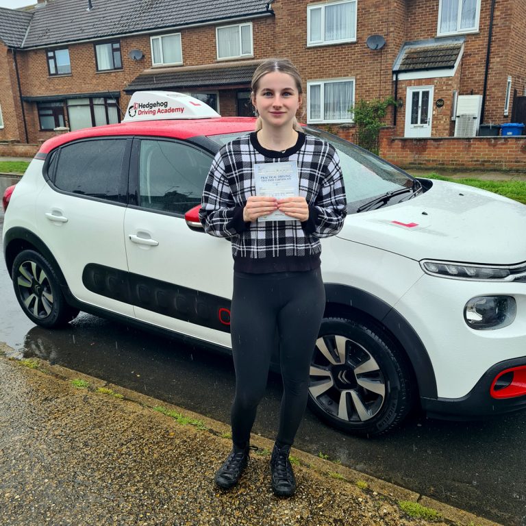 A student holding their pass certificate in front of the Hedgehog Driving Academy car