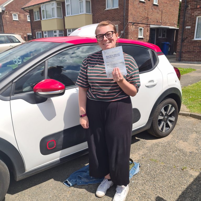 A student holding their pass certificate in front of the Hedgehog Driving Academy car