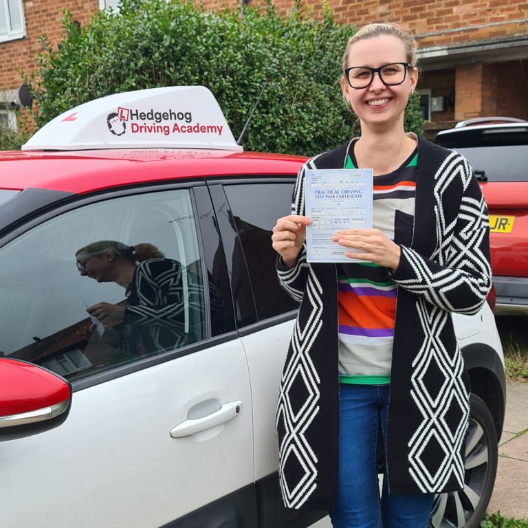 A student holding their pass certificate in front of the Hedgehog Driving Academy car