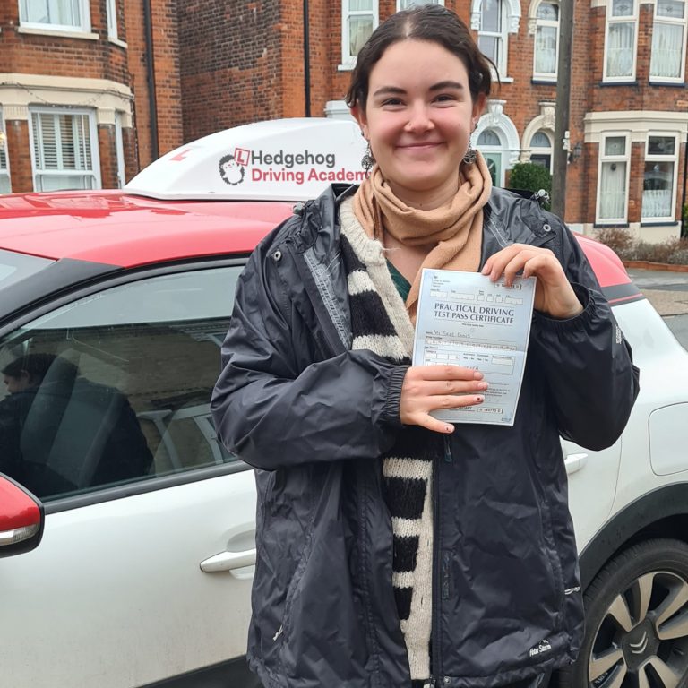 A student holding their pass certificate in front of the Hedgehog Driving Academy car